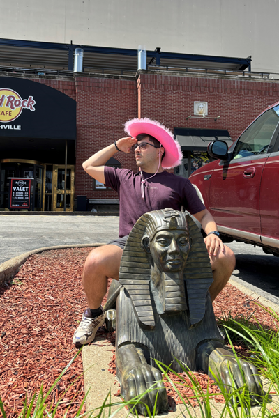 Male resident wearing a pink cowboy hate while sitting outside on a sphynx statue outside Hard Rock Cafe