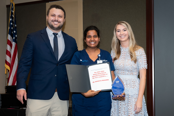 Two female and a male resident holding an award