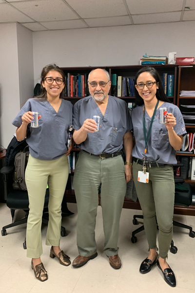 Fellows and faculty standing in an office holding Pepsis