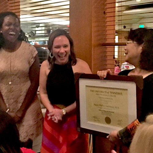 Two female fellows receiving a certificate from faculty at graduation