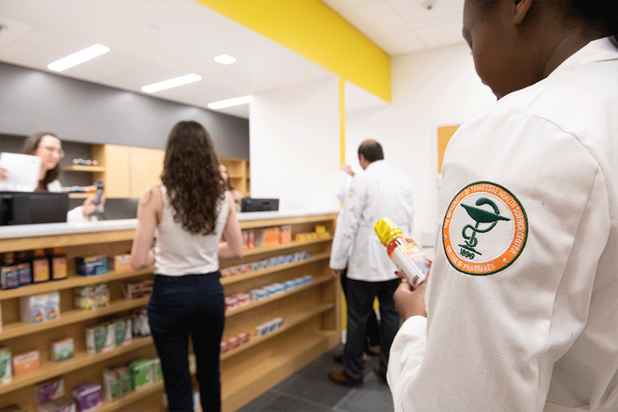 Pharmacy setting with a student with a pharmacy badge on coat in the foreground.